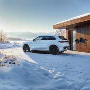 Q5 e-hybrid sedd från sidan. Står parkerad bredvid ett trähus i vinterlandskap med berg i bakgrunden.